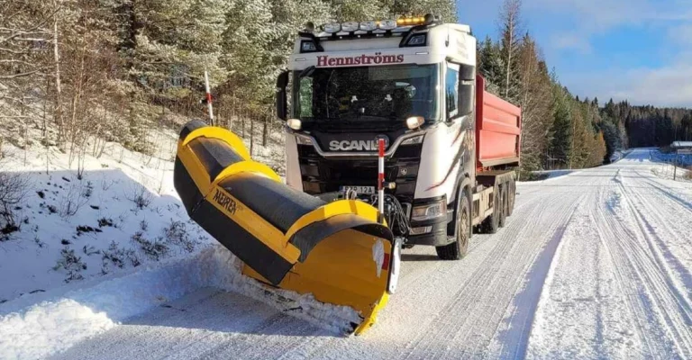 Hennströms plogbil med vikplog röjer en snöig skogsväg
