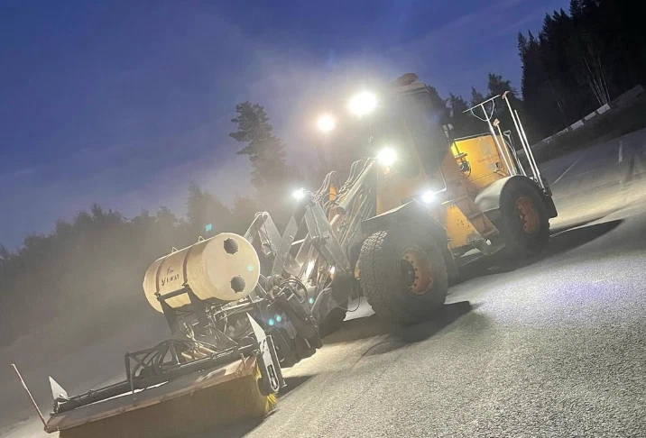 Hjullastare med spridare halkbekämpar en väg en vinterkväll