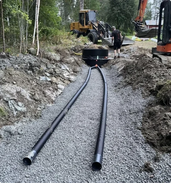 Två dräneringsrör i grusbädd fram till nedgrävd tank, hjullastare i bakgrunden