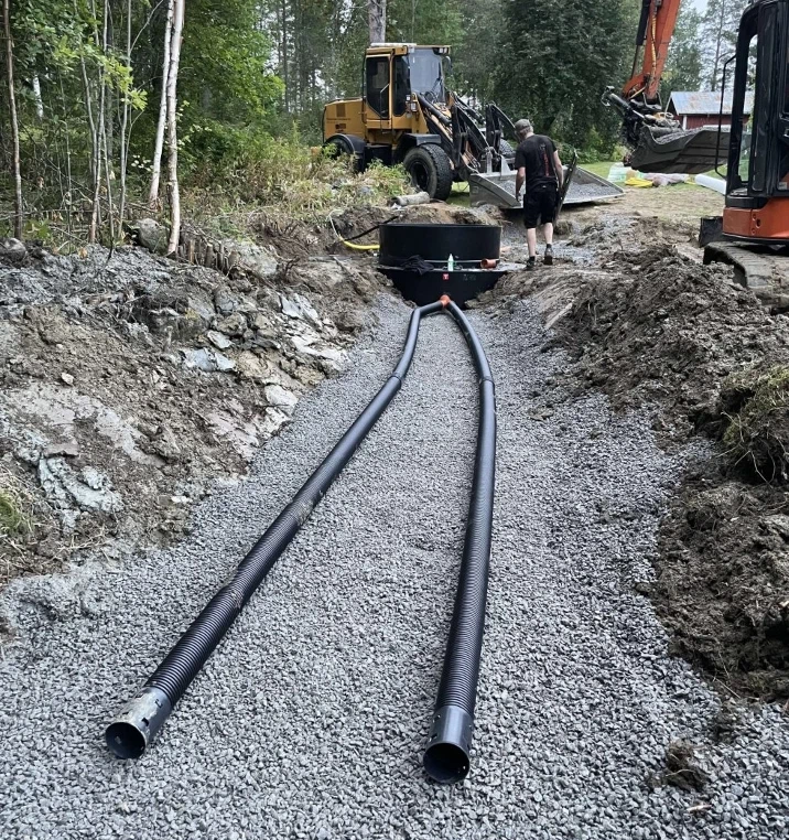 Två avloppsrör i grusbädd fram till en nedgrävd tank, hjullastare i bakgrunden