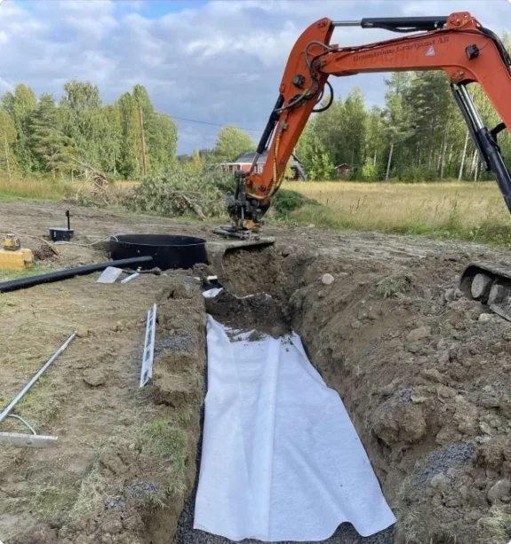 Hennströms grävmaskin lägger fiberduk i schakt för avloppsanläggning