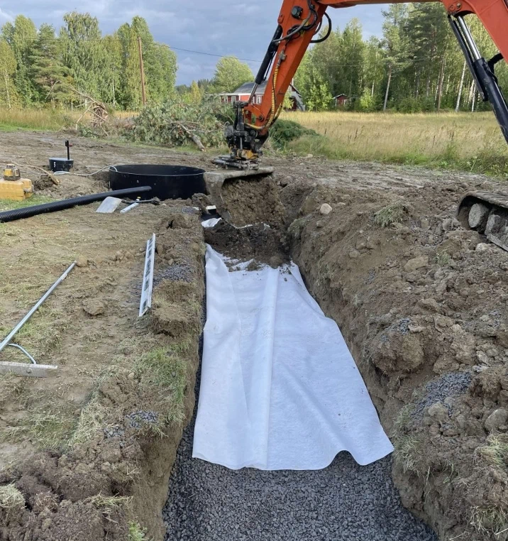 Grävmaskin lägger fiberduk i schaktet för en ny avloppsanläggning